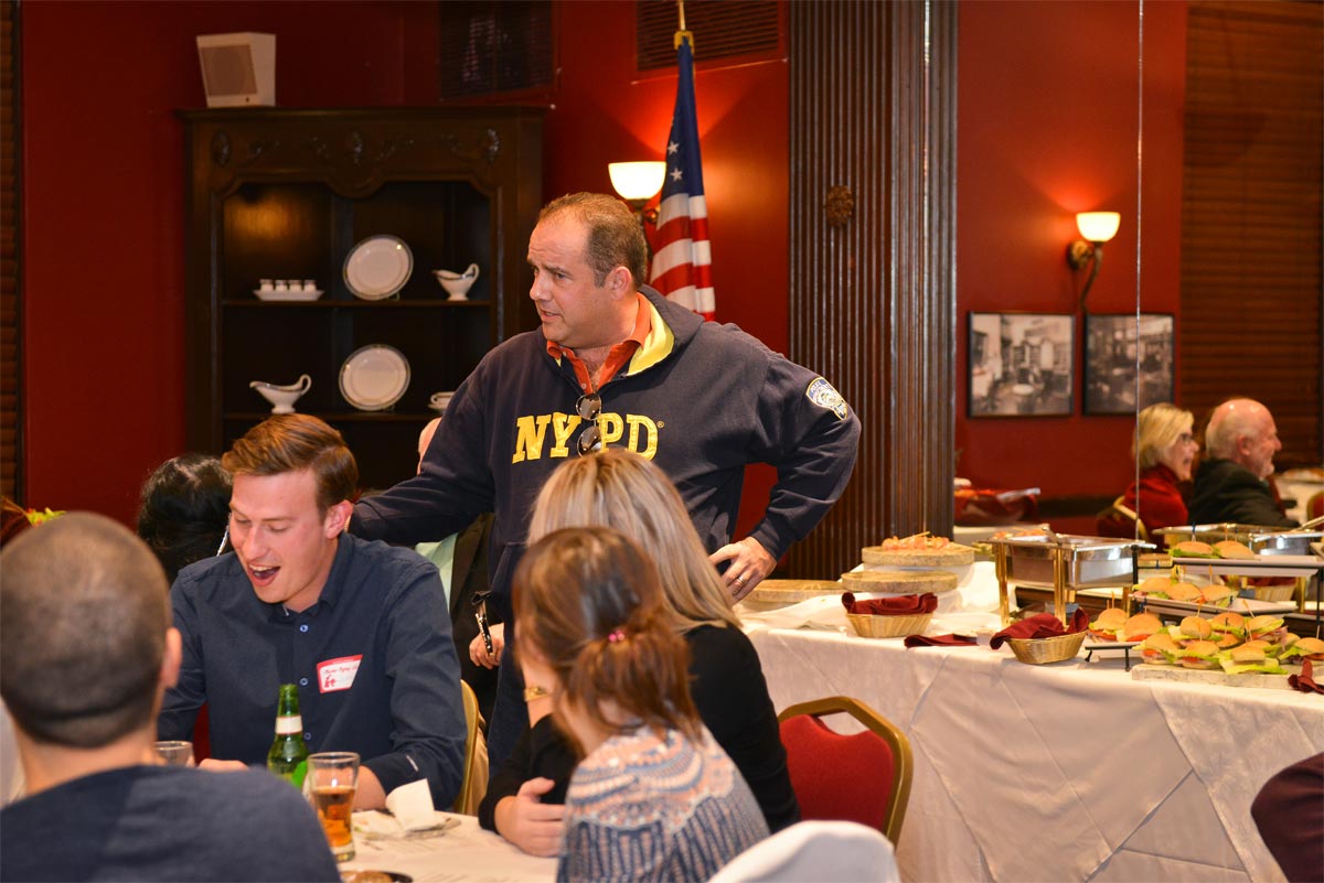 A man in an NYPD jacket addressing a dining room full of people