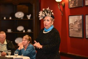 A woman in an elaborate hat, speaking to a group